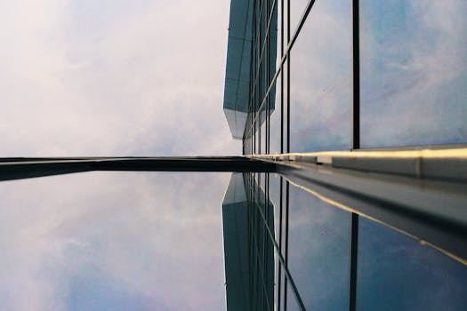 低角度拍摄的现代玻璃建筑映照着天空，展现了城市环境中的当代建筑设计