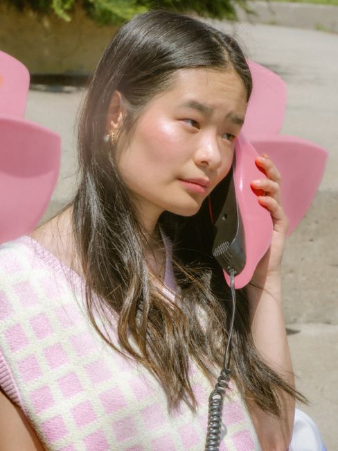 Young Asian woman with retro analog phone in vibrant summer setting.