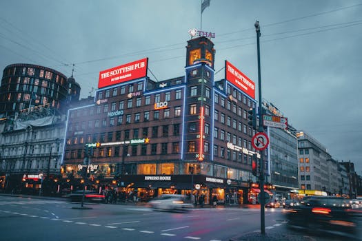 A bustling city street featuring lit facades and lively evening activity.