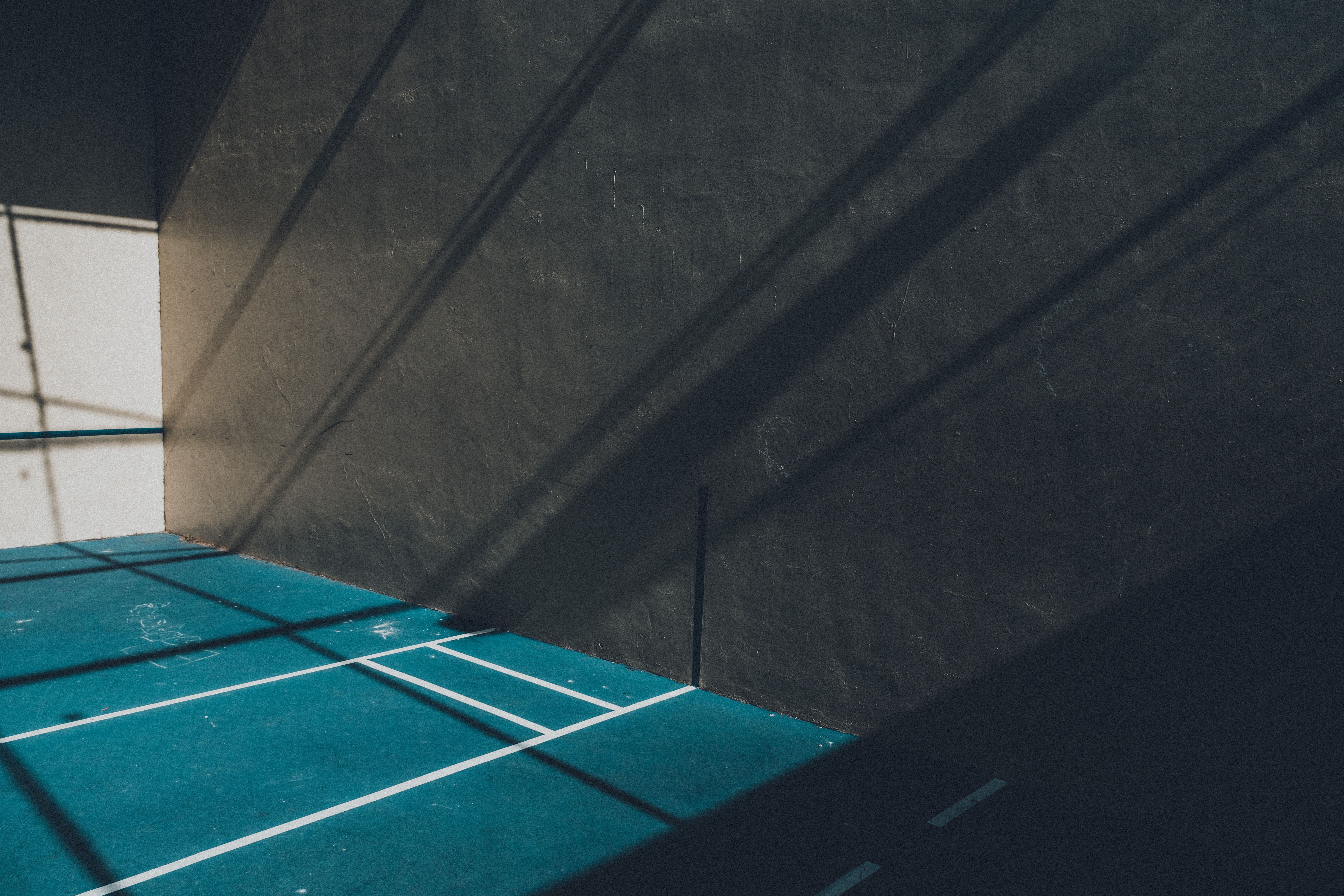 Dramatic shadows cast on an empty indoor squash court with blue flooring, creating a striking visual.