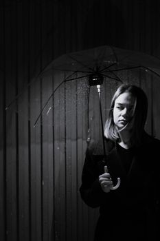 A dramatic black and white portrait of a woman holding an umbrella in the rain.