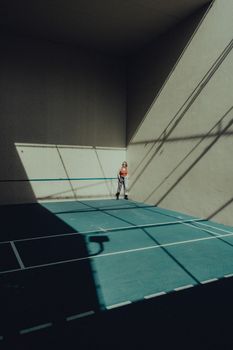 Woman standing in a shadowed outdoor court with sunlight casting geometric patterns.