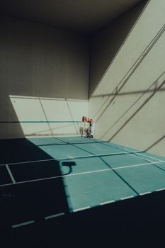 A woman stands on a tennis court with shadows and sunlight creating dramatic patterns.