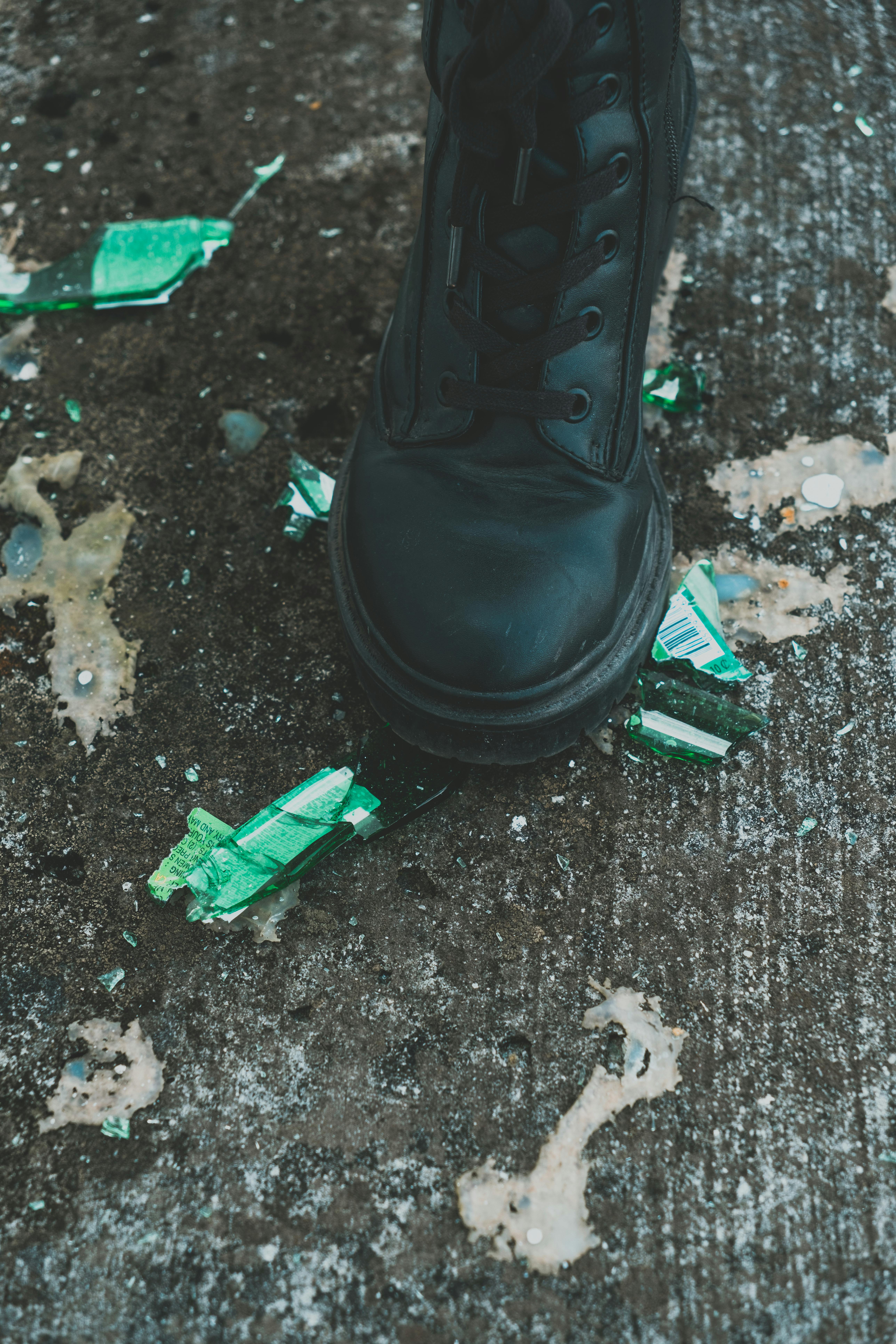 close up photo of black boots near broken glass