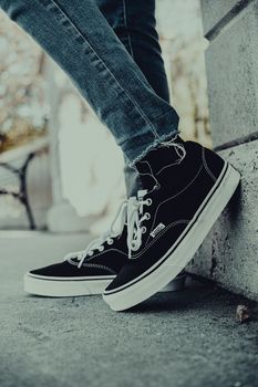 Close-up of person wearing sneakers, leaning against a wall in urban setting.