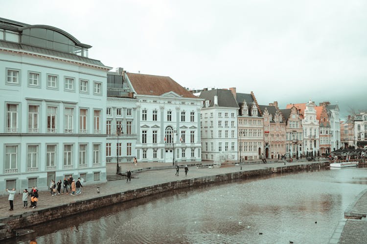 An Aerial Photography Of People Walking On The Street Between River And Buildings