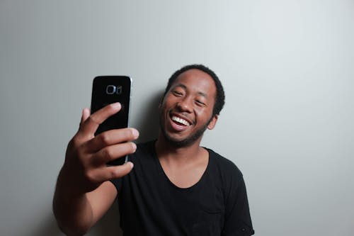 Free Man Holding Smartphone While Leaning on White Wall Stock Photo