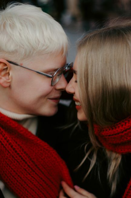 Joyful couple sharing a moment outdoors, wrapped in red scarves, showcasing warmth and connection.