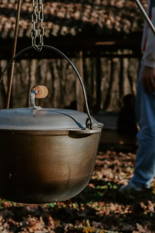 Free Close-up of a hanging pot with a chain in a sunlit forest area, suggesting outdoor cooking. Stock Photo