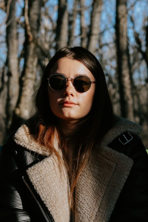 Free Portrait of a woman wearing sunglasses in a sunlit forest during autumn. Stock Photo