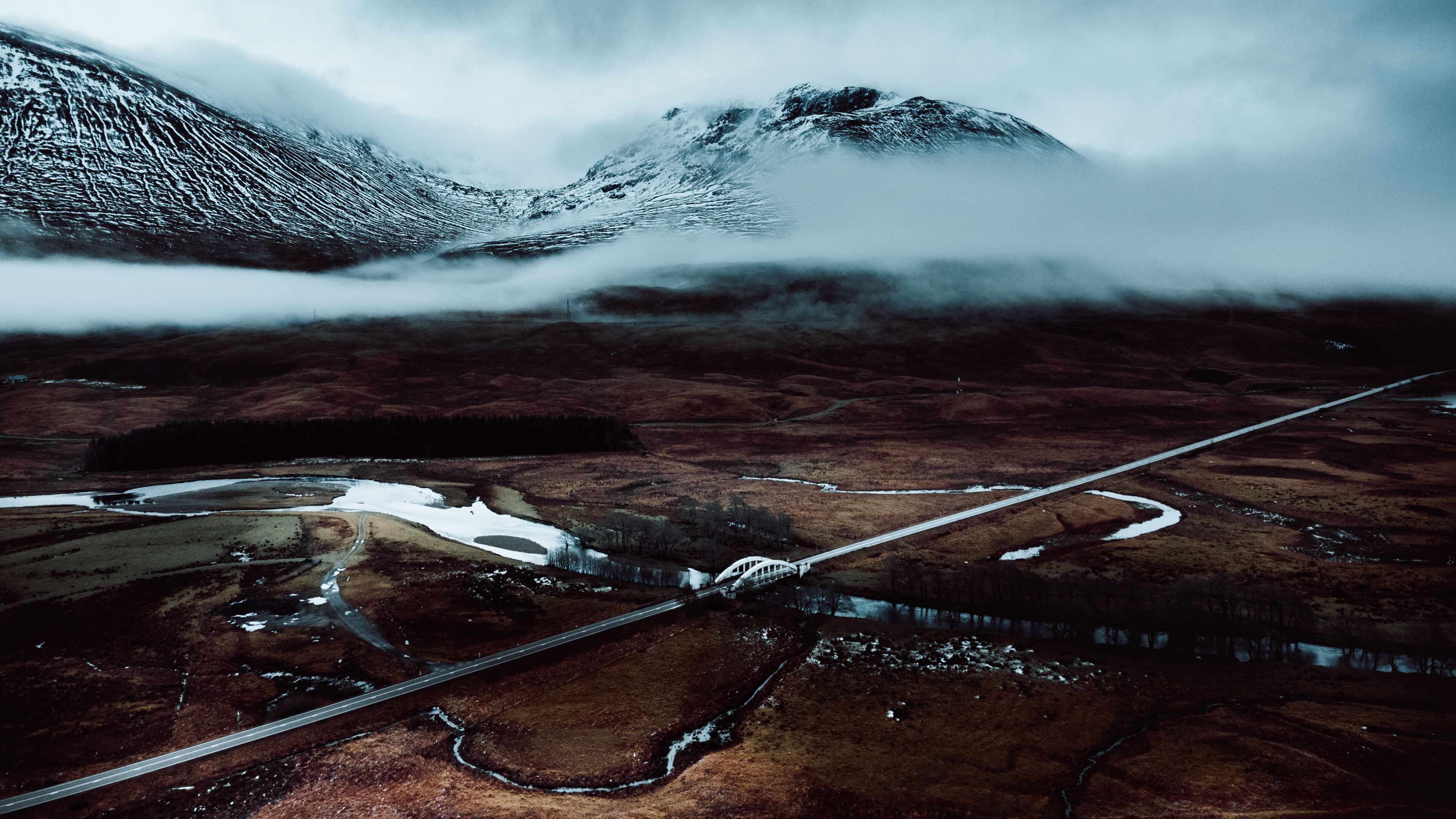 A road running straight across snow-covered peat moor below snowy mountains