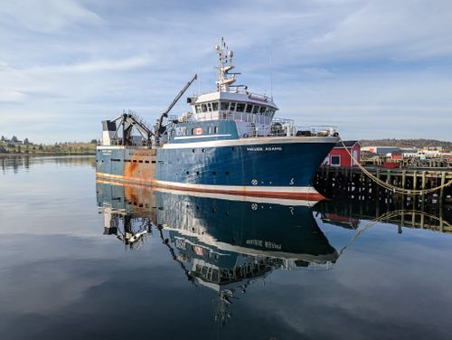 Free A fishing vessel docked in Lunenburg Harbor, Nova Scotia, reflecting on calm waters. Stock Photo