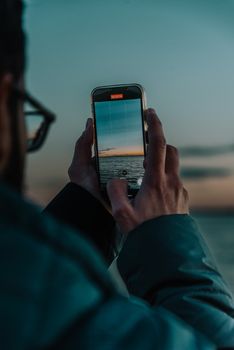 A person photographing a stunning sunset over the ocean with a smartphone.