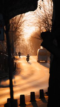A serene urban street scene in Turkey at sunset, featuring a motorbike and a mini bus amidst bare trees.