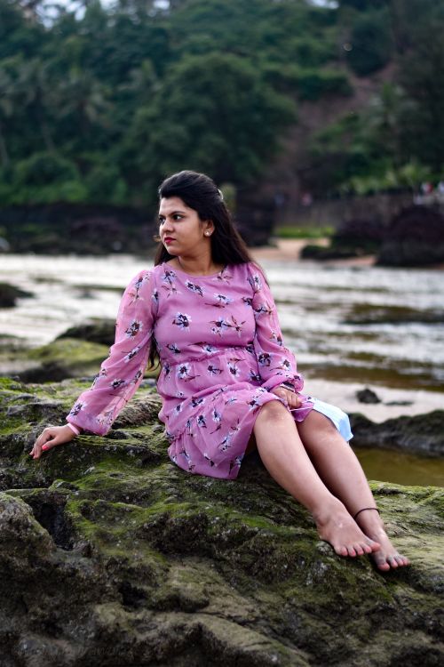 Free Woman in a pink floral dress sitting barefoot on rocks by the river in rural India, enjoying nature. Stock Photo