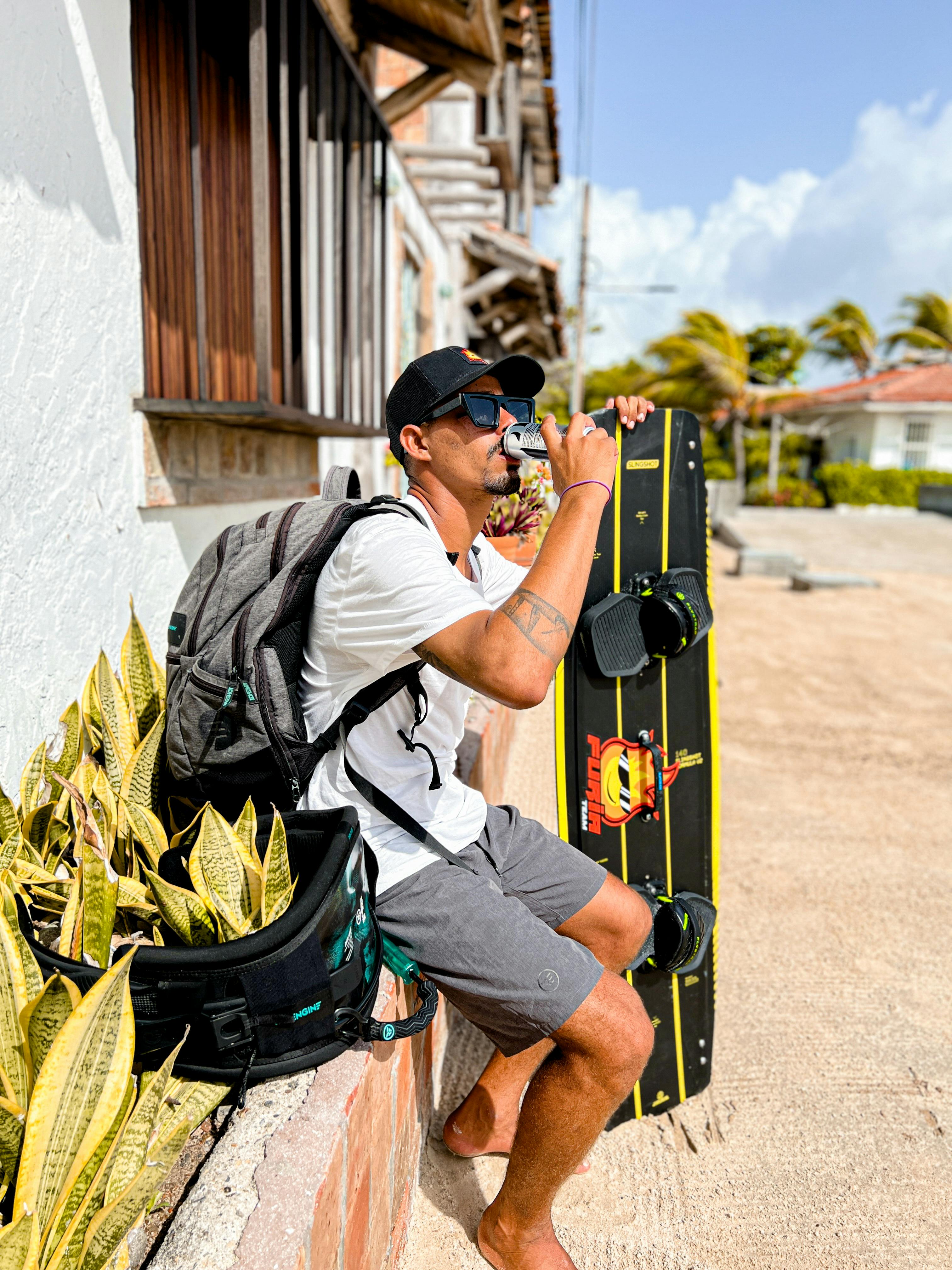 Free Man sitting outdoors sipping drink, holding surfboard on a sunny day. Stock Photo