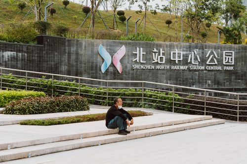 Free An Asian man sits on steps at Shenzhen North Railway Station Central Park, a tranquil urban setting. Stock Photo