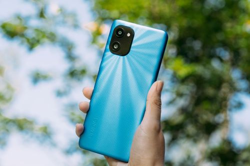 Free Close-up of a hand holding a blue smartphone, vibrant outdoor setting. Stock Photo