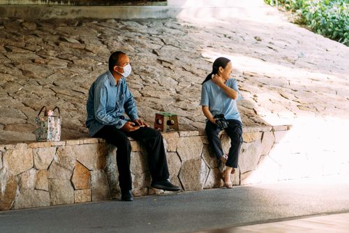 Free A couple sitting outdoors on a stone bench, enjoying a sunny day. Stock Photo