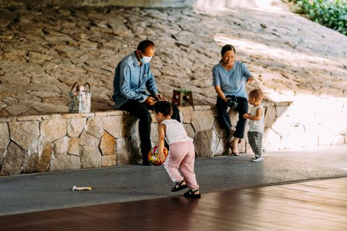 Free Two children playing with a ball under parental supervision outdoors, conveying joy and family bonding. Stock Photo