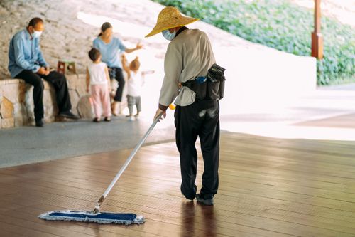 Free A person mopping an outdoor wooden floor in a park setting with others in the background. Stock Photo