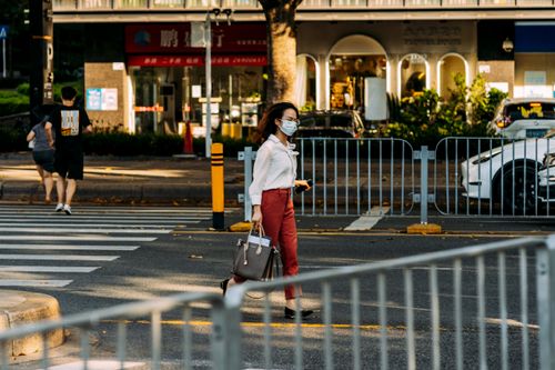 Free Masked woman walking across a city street, showcasing urban life and safety precautions. Stock Photo