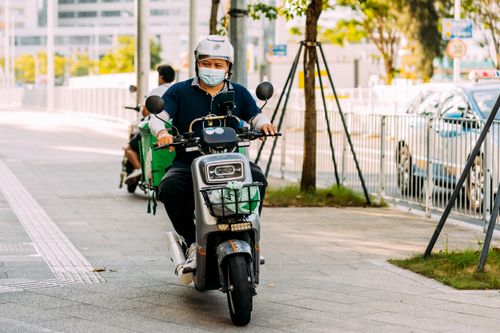 Free A delivery person riding a scooter with a helmet and facemask on a city street. Stock Photo