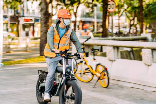 Free Construction worker commuting on a bike in a busy city street wearing a safety vest and helmet. Stock Photo