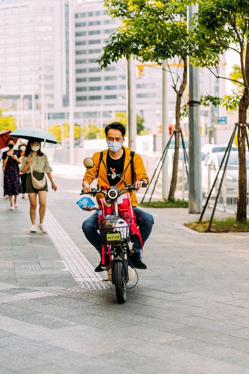 Free A city street scene with pedestrians and a biker wearing a mask during daylight. Stock Photo