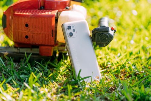 Free A smartphone leaning against a red machine on a grassy field, showcasing technology in an outdoor setting. Stock Photo