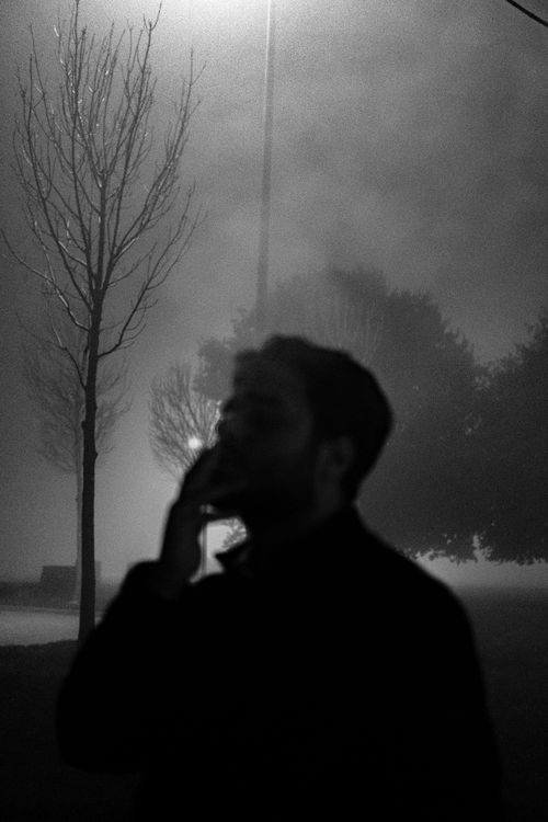 Free A silhouette of a man smoking in a foggy park at night, creating a mysterious and moody atmosphere. Stock Photo