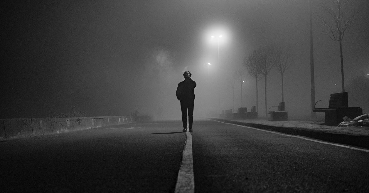 Silhouette of a person standing in a mysterious, foggy forest with a vintage car