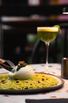 Tantalizing gourmet dish of creamy burrata on green risotto paired with an elegant cocktail.