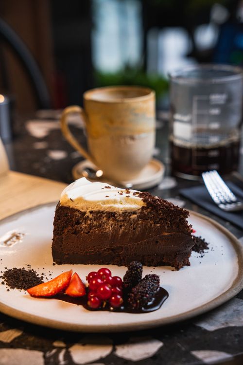 Free Indulge in a rich chocolate cake slice paired with fresh fruits at a warm, inviting cafe. Stock Photo