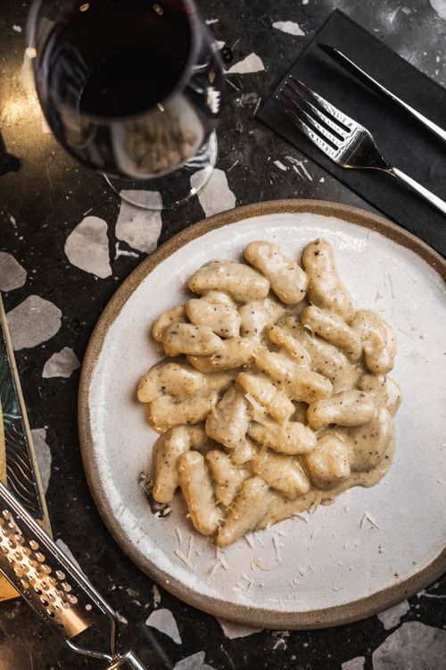 Free Close-up of creamy gnocchi with a glass of red wine on a marble table, perfect culinary delight. Stock Photo