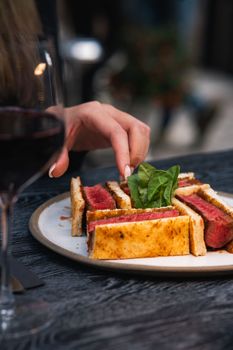 Close-up of a gourmet steak sandwich with a glass of red wine, perfect for fine dining.