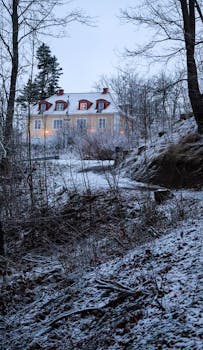 A serene snowy mansion nestled in a winter forest during dusk, creating a peaceful atmosphere.