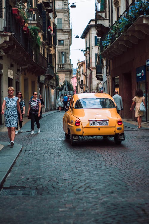 Free Yellow Sedan on Road While People Walking on Sidewalk Stock Photo