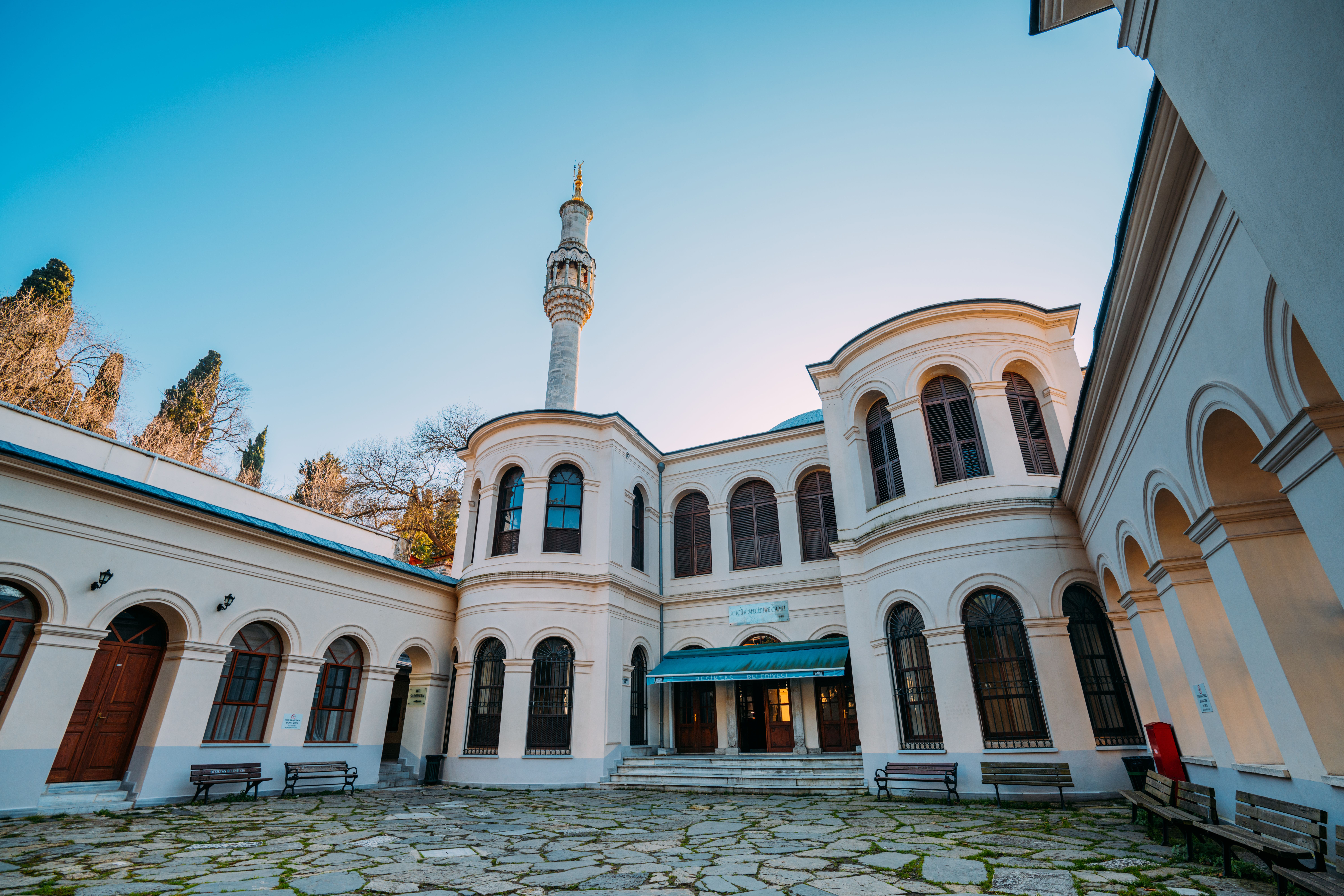 A beautiful mosque courtyard with a classic facade and towering minaret under the clear evening sky.