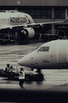 Black and white image of airplanes on runway with workers, showcasing a busy airport atmosphere.