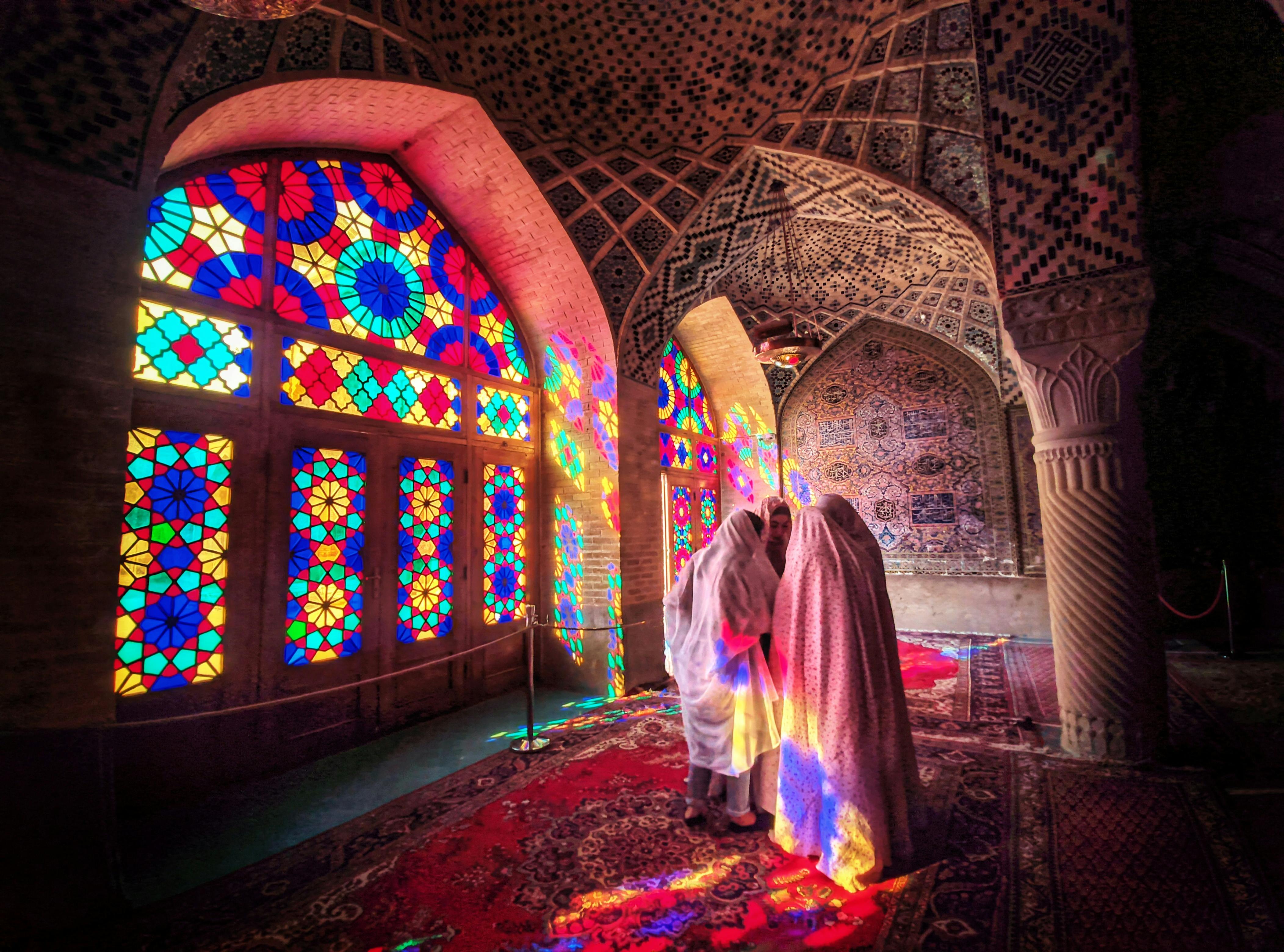 group of women in chadors in front of the colorful stained glass window of the pink mosque