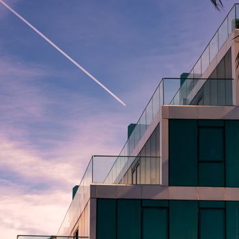 Contemporary urban architecture with a jet contrail against a blue sky.