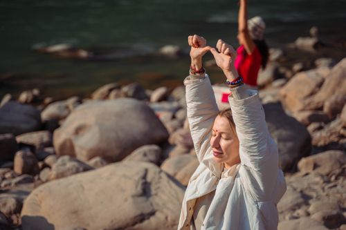 Free Relaxing by the Rishikesh river, a woman practices mindful meditation on rocky shores. Stock Photo