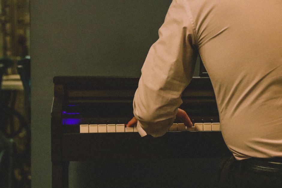 A man wearing a shirt playing piano indoors, focus on hands.