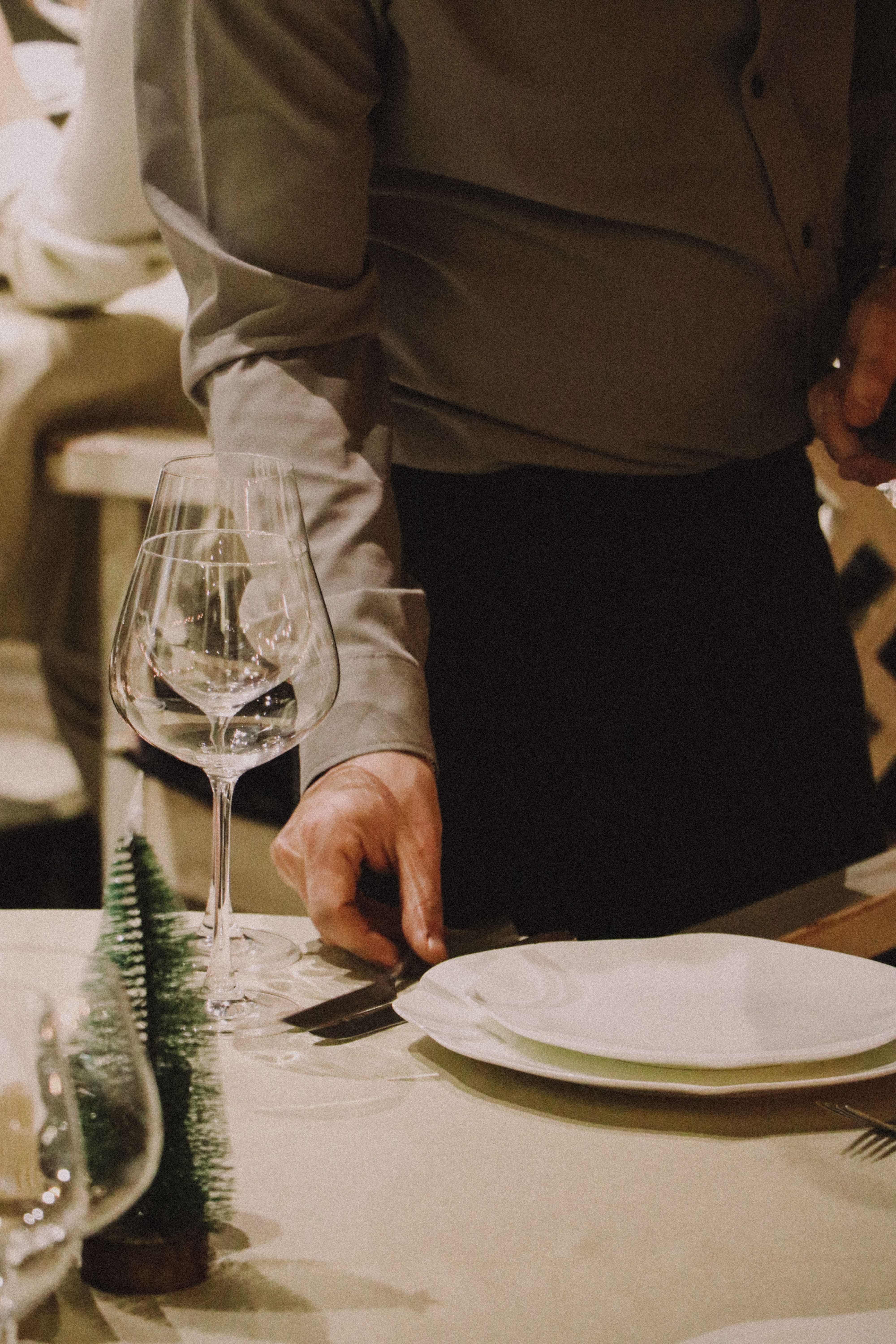 A close-up of a table setting featuring glassware and plates with a hand arranging cutlery.