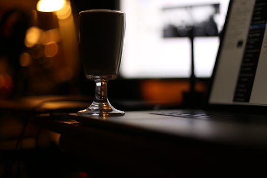 A moody workspace scene featuring a drinking glass and laptop with ambient lighting.