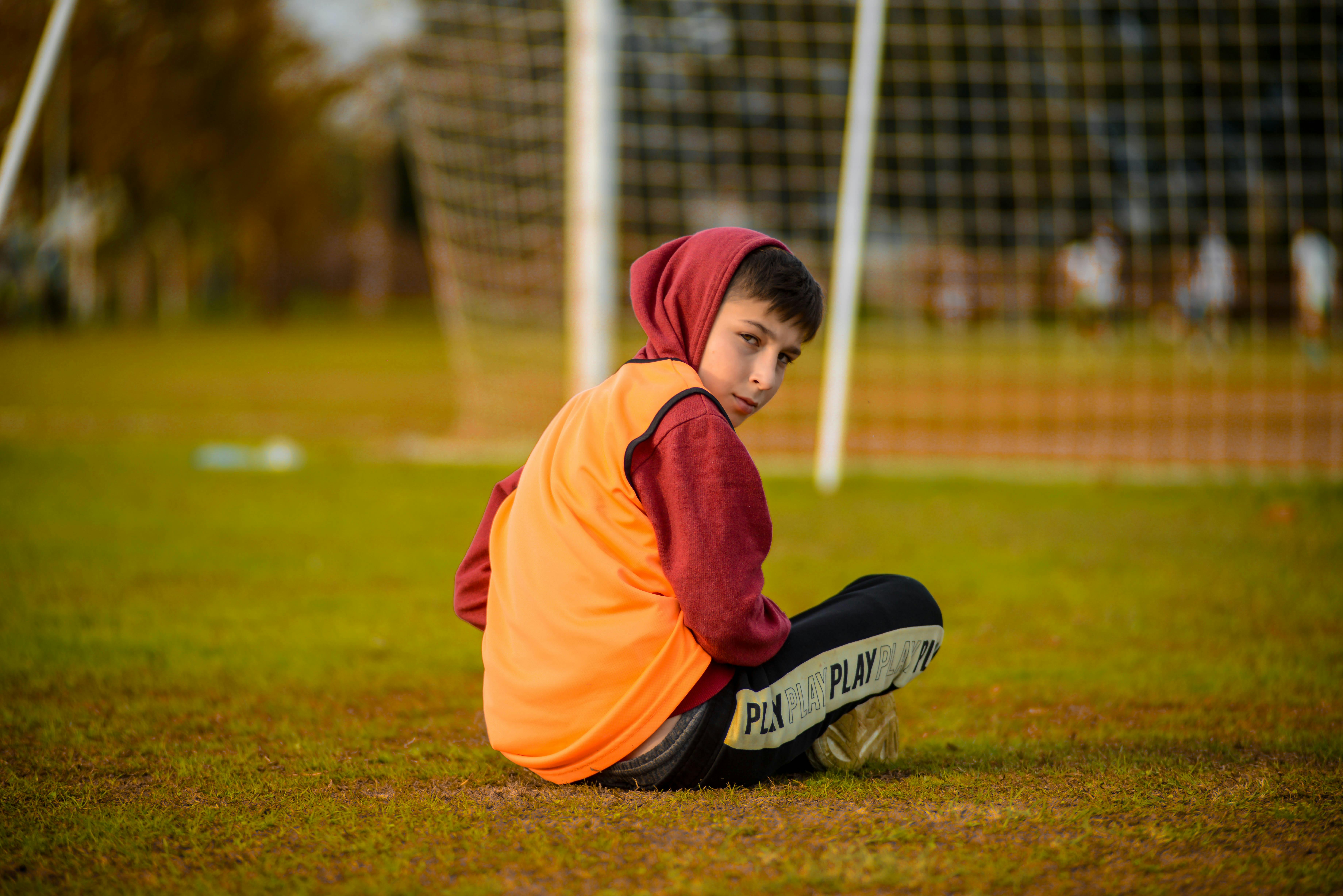 boy in a hoodie sitting on the grass by the goal