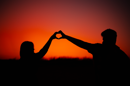 Free Silhouette of a couple forming a heart shape with hands during a romantic sunset. Stock Photo