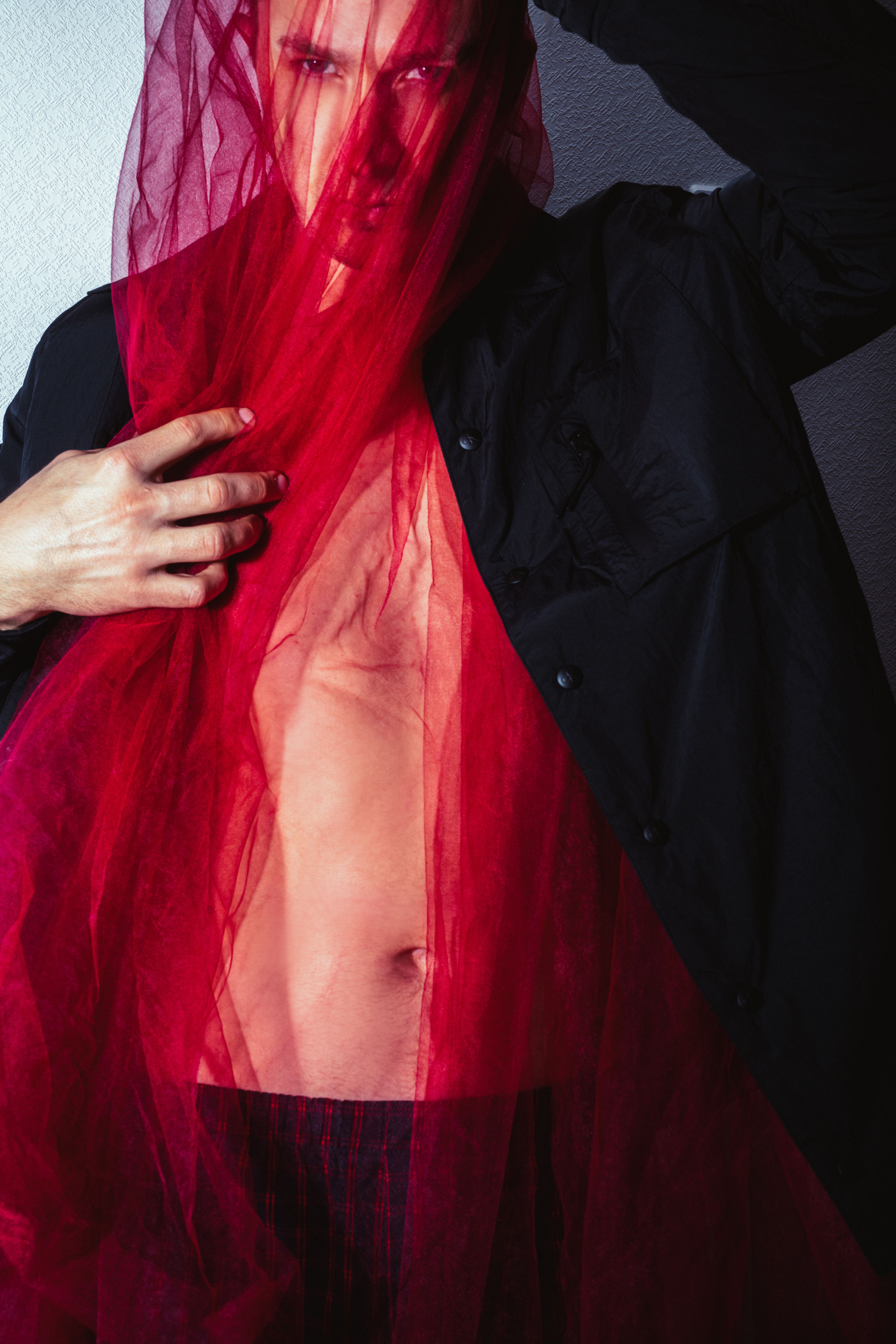 Artistic portrait of a male model posing with a vibrant red veil, showcasing contemporary fashion and elegance.