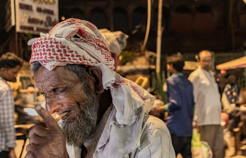Free Portrait of an elderly man with a headscarf smoking at a night market in New Delhi, India. Stock Photo